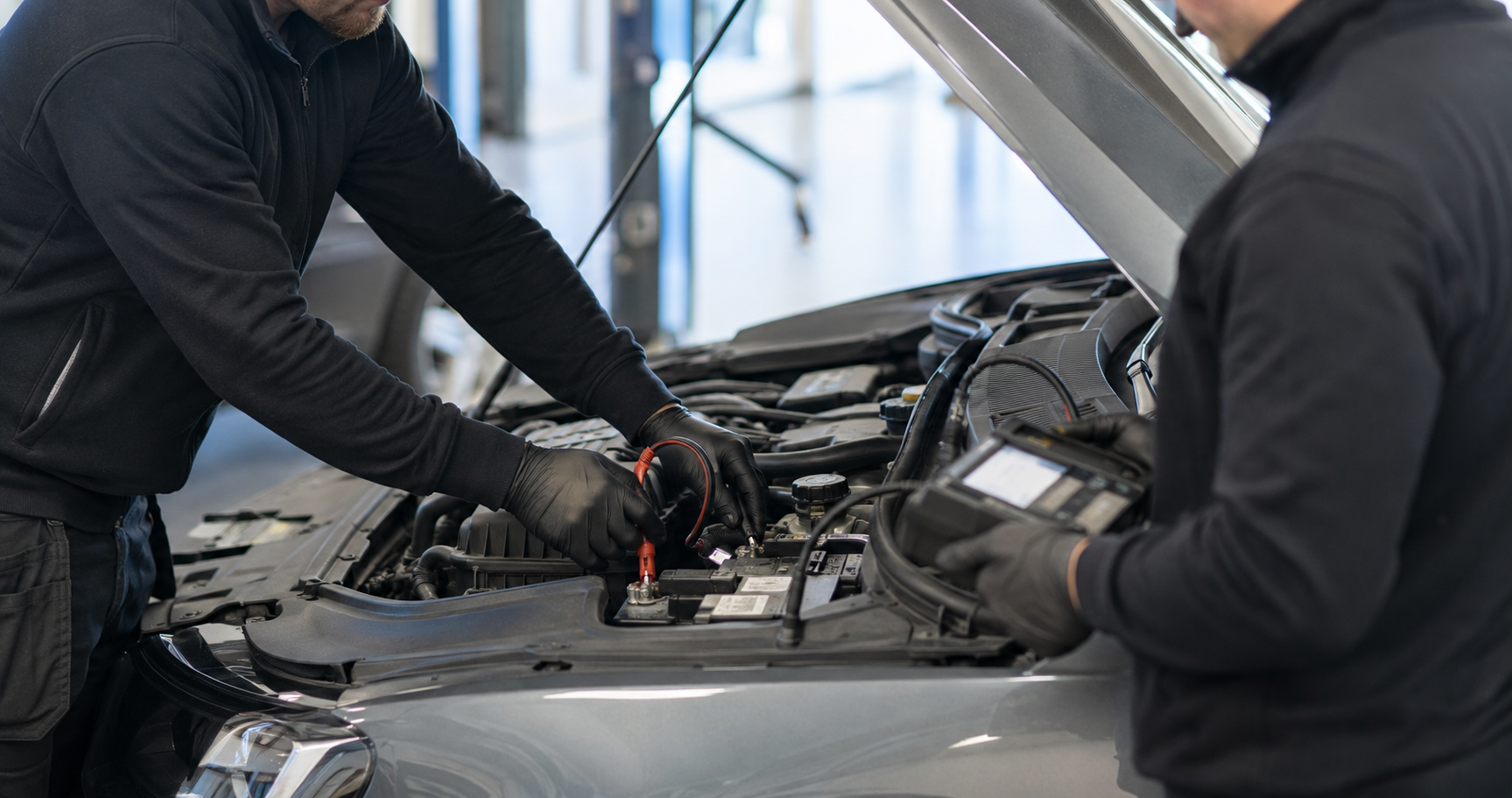 Två mekaniker testar en bils batteri under motorhuven